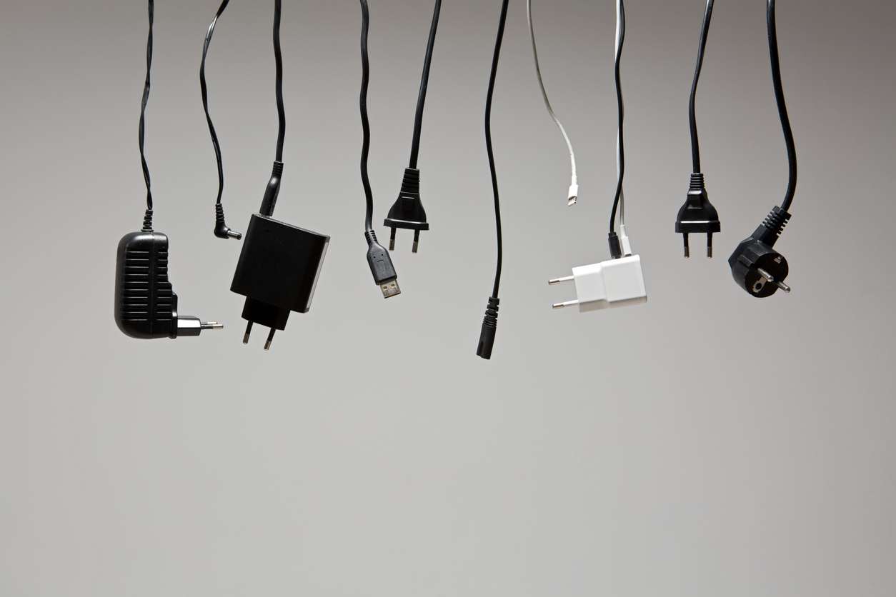 Different cables with plugs that need the right voltage converters hanging in a row against a neutral background